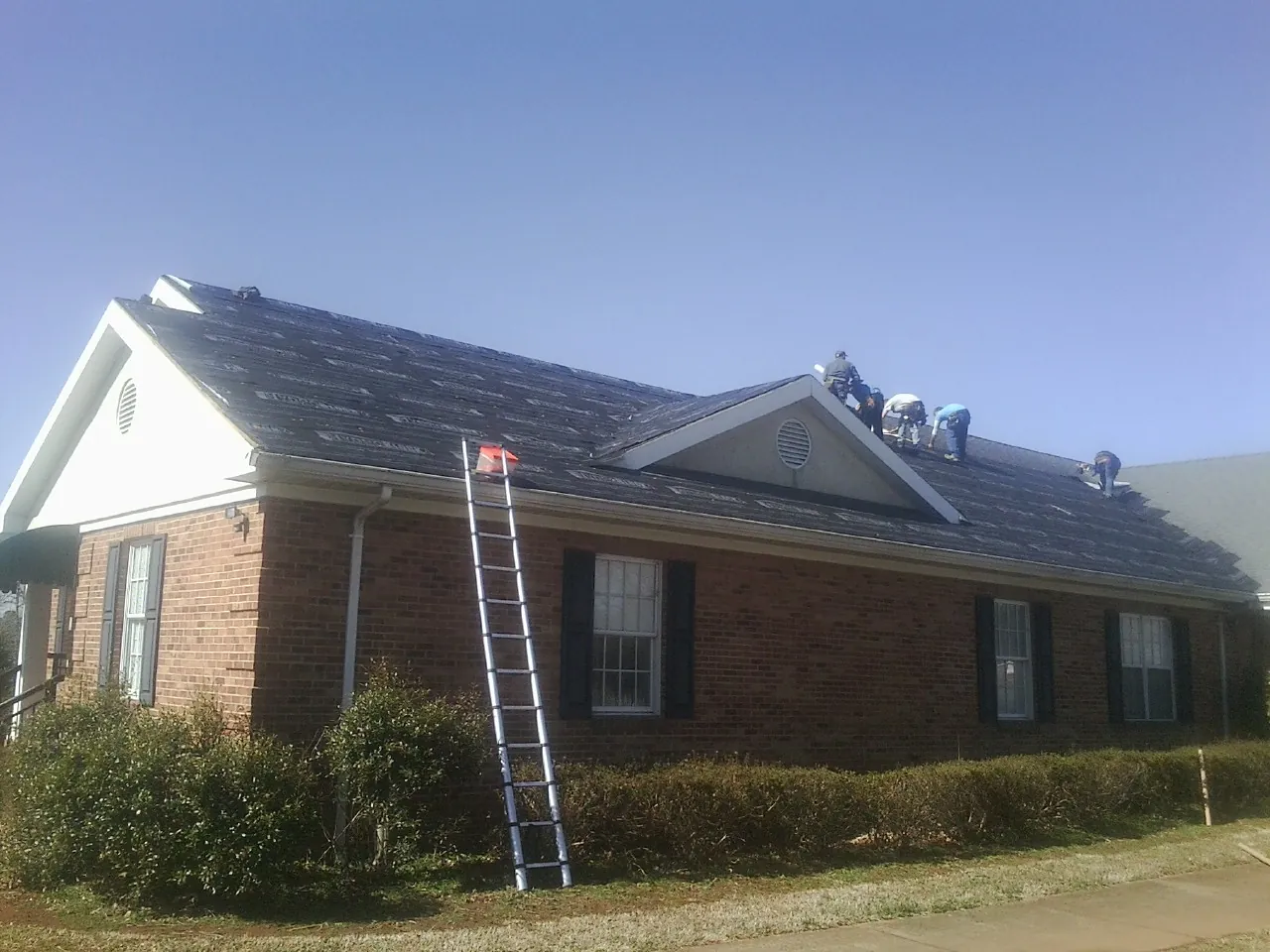 Crew tearing shingles off a brick ranch roof with a ladder set — Emergency Roof Repair work by our crew in Freeport