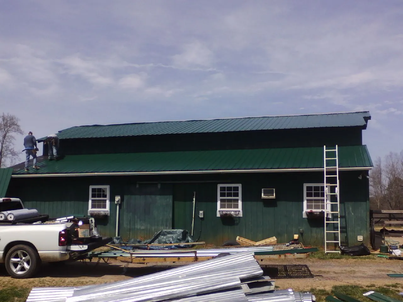 Crew installing green metal roofing on a large green barn in Freeport